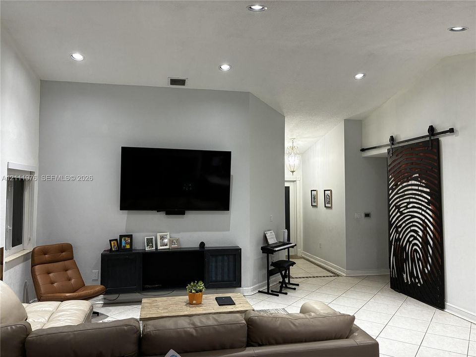 High-ceilinged living area featuring recessed lighting, neutral wall finishes, tile flooring, and a decorative sliding barn door with custom detailing