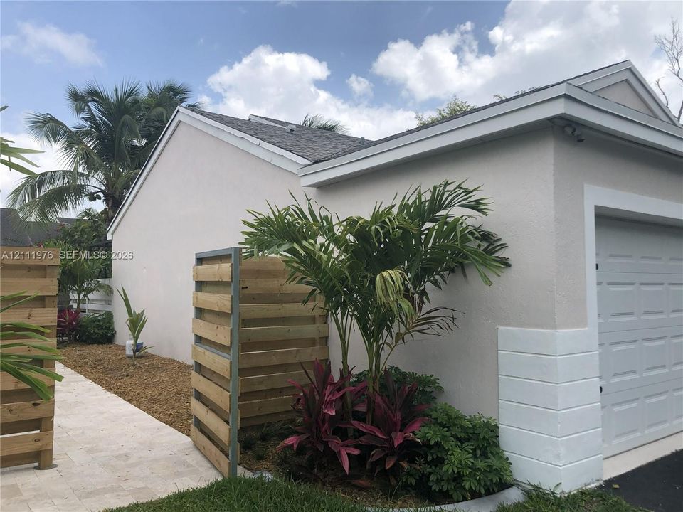 Stucco exterior featuring horizontal wood-slat privacy fencing, a paver walkway, and a multi-panel garage door with masonry detailing