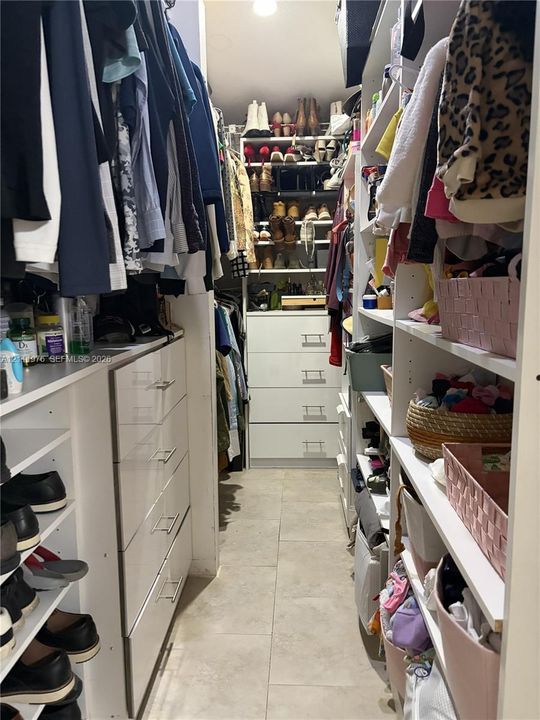 Custom walk-in closet featuring white built-in shelving, floor-to-ceiling storage cabinetry with pull-out drawers, and tile flooring