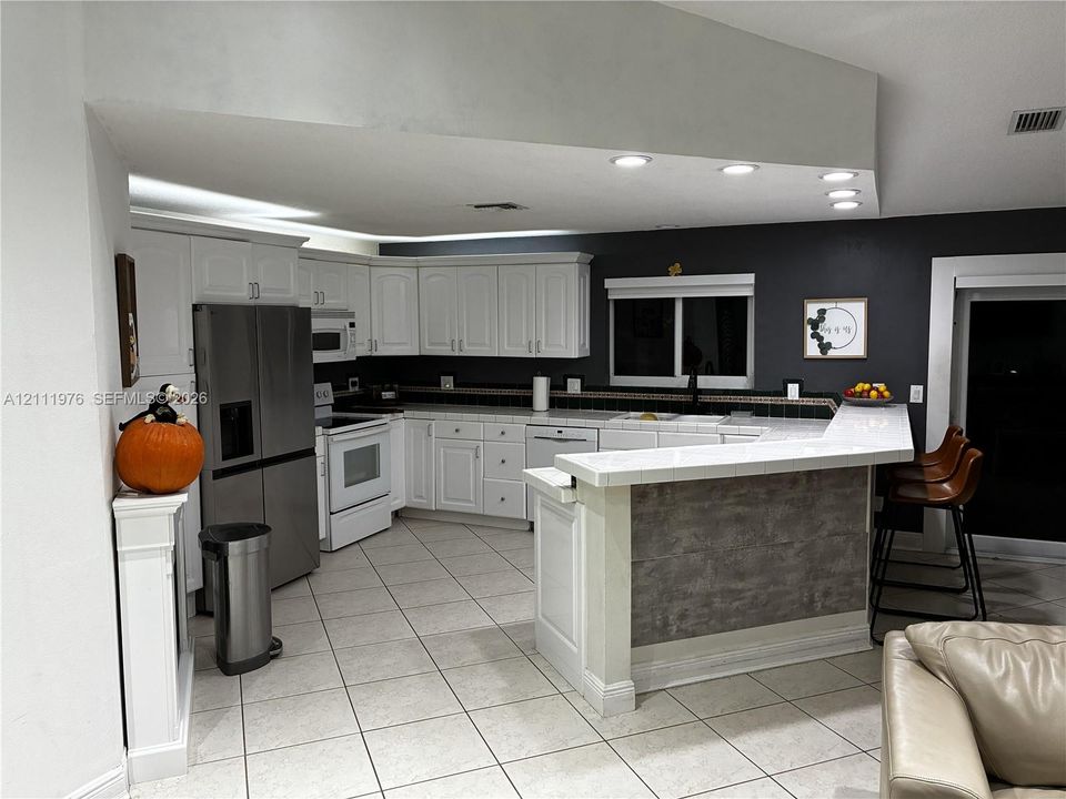 Kitchen featuring white cabinetry, tiled countertops, stainless steel refrigerator, recessed lighting, and a breakfast bar with textured finish