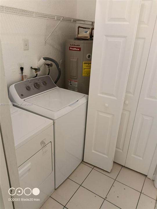 Laundry area featuring white tile flooring, built-in overhead wire shelving, and bi-fold closet doors