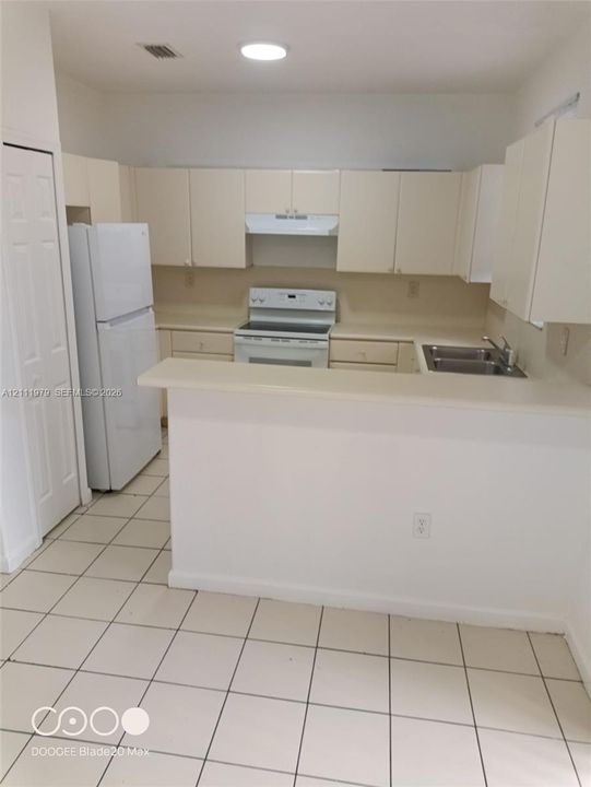 Kitchen featuring a peninsula counter, tile flooring, cabinetry, built-in dual-basin sink, and white appliances