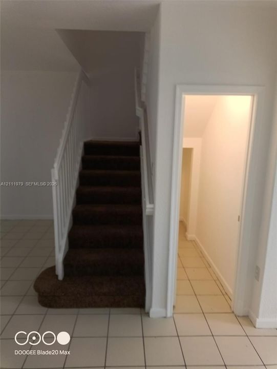 Staircase featuring a carpeted runner, white painted railing, and tiled flooring