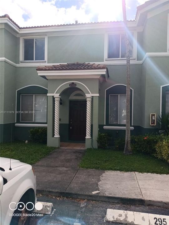 Exterior featuring a two-story stucco facade, arched entryway with decorative spiral columns, tile roof accents, and landscape shrubbery