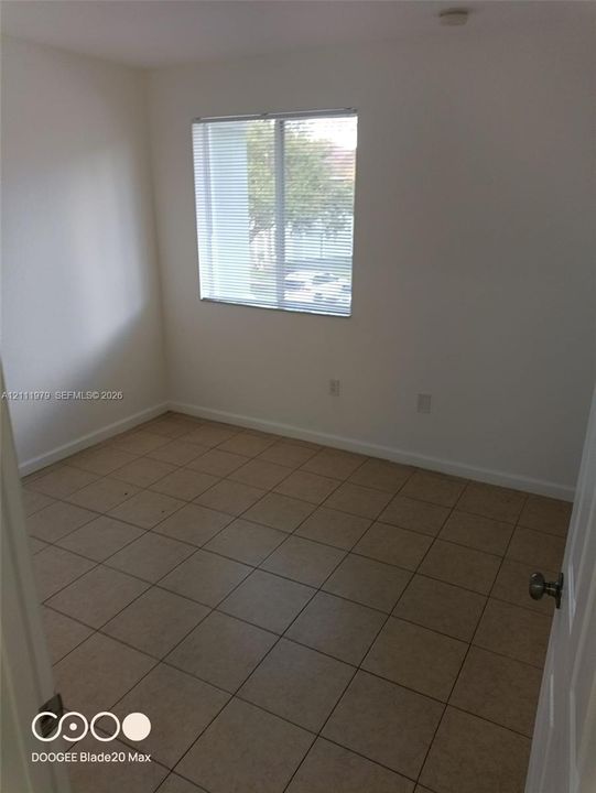 Neutral-toned ceramic tile flooring, solid wall construction, and a single window with horizontal blinds