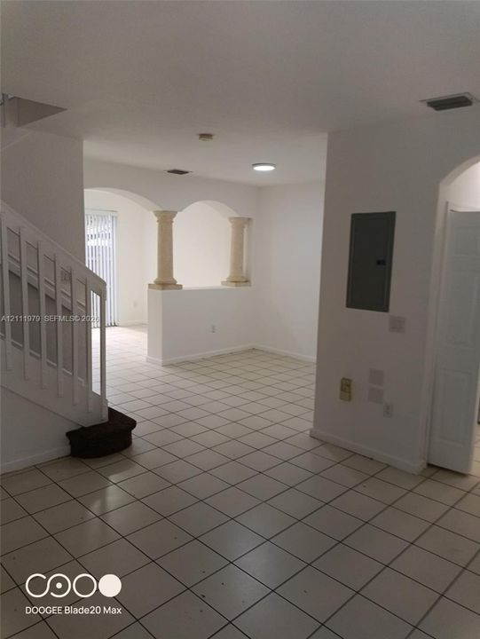 Interior space featuring neutral tile flooring, decorative architectural columns, arched wall openings, and a staircase with a white railing