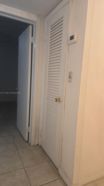 White louvered closet door featuring a brass-finished knob and digital thermostat