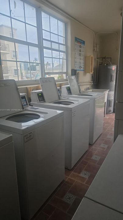 Laundry area featuring large-format multi-unit washer stations, a utility sink, oversized grid-pane windows, and ceramic tile flooring