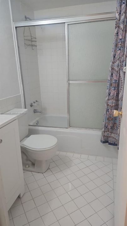 Bathroom featuring a white vanity, a standard toilet, and a combined tub and shower enclosure with a sliding glass door and tiled surround, finished with white diamond-patterned floor tile