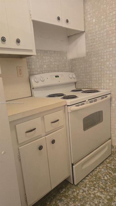 Kitchen featuring white cabinetry, an electric range, solid surface countertops, and square tile backsplash