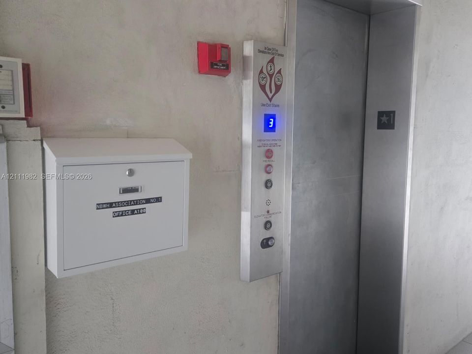 Elevator access with stainless steel panel and wall-mounted white locking mailbox