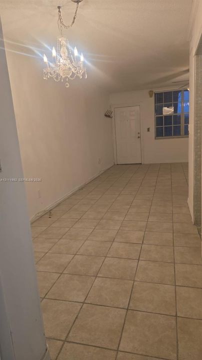Interior area featuring neutral square tile flooring, a multi-arm chandelier with crystal accents, and a grid-pane window