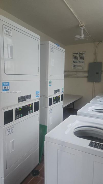 Laundry facility featuring multiple stacked commercial-grade washer and dryer units, a folding table, and tiled flooring
