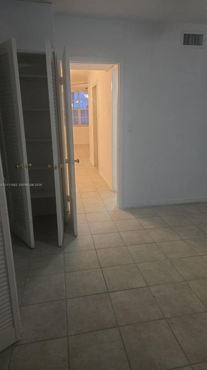 Neutral-toned tile flooring, built-in storage closet with louvered doors, and light-colored interior walls