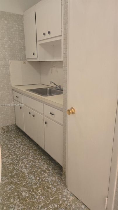 Kitchenette featuring white cabinetry, a neutral-toned countertop, a stainless steel sink with a chrome faucet, mosaic wall tiling, and patterned tile flooring