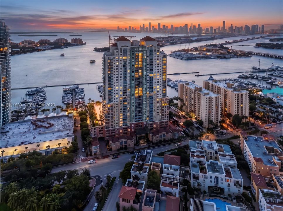 Aerial perspective of a high-rise residential tower featuring a multi-story masonry facade, terracotta-tiled roof accents, private balcony tiers, and a waterfront location