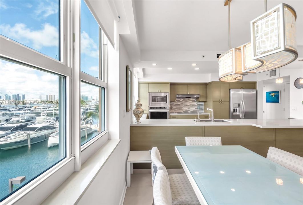 Kitchen featuring flat-panel cabinetry, quartz countertops, stainless steel appliances, multi-toned tile backsplash, and oversized glass pendant lighting