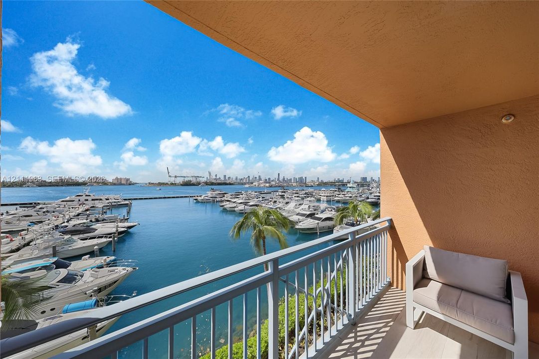 Covered balcony featuring stucco walls, metal railings, and stone-finish flooring, overlooking a marina and city skyline