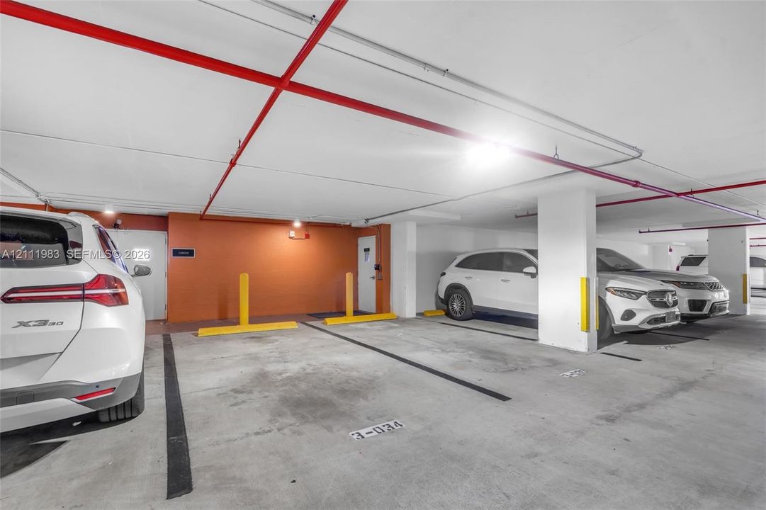 Covered parking garage featuring concrete flooring, structural support pillars, assigned space markers, and high-visibility wheel stops