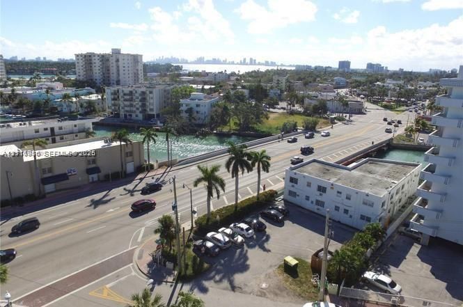 Aerial perspective featuring coastal surroundings, a waterway, multi-story urban structures, palm trees, and a metropolitan skyline in the distance