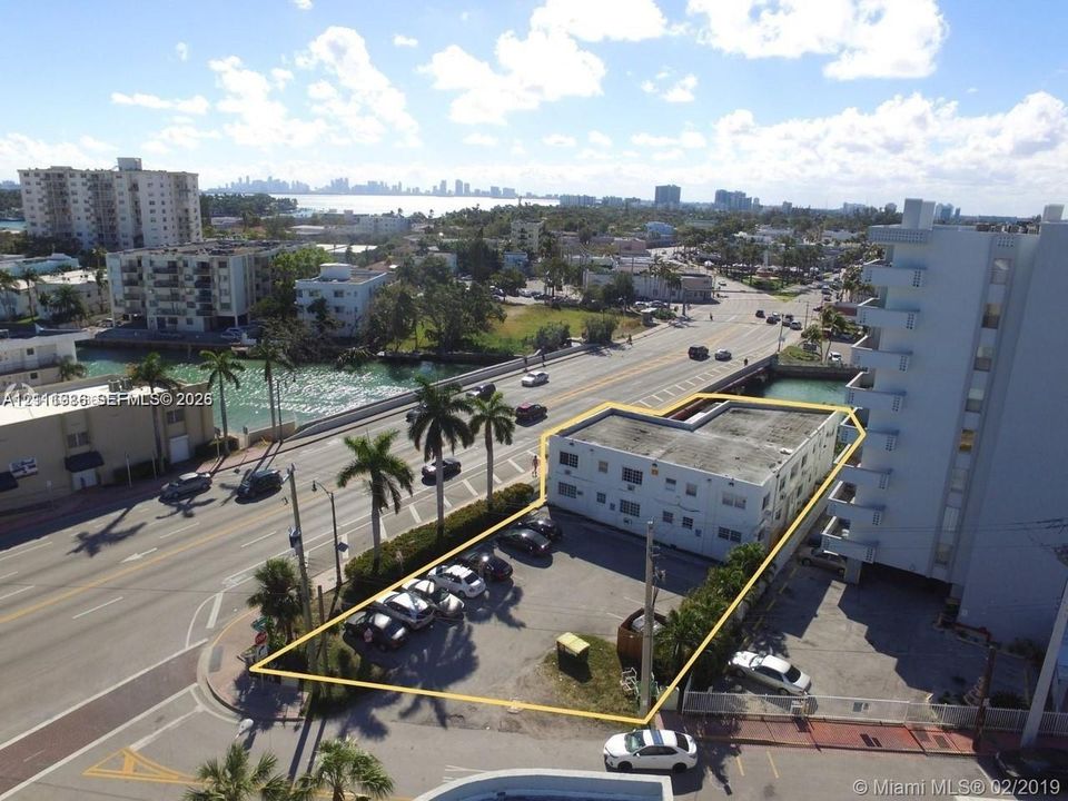 Aerial perspective of a multi-unit property featuring an asphalt parking lot, perimeter landscaping, and frontage on a primary thoroughfare