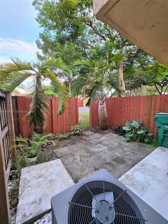 Concrete patio area featuring a wooden privacy fence, metal balcony railing, and exterior wall-mounted lighting