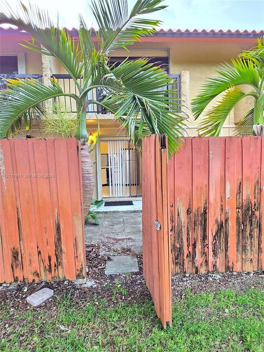 Private patio featuring square concrete pavers, enclosed by wood fencing, and accented by mature palm trees and established landscaping