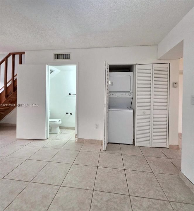Open-concept living space featuring large-format tile flooring, a prominent wooden staircase with open balusters, dual bi-fold closet doors, and a kitchen pass-through window with an attached counter