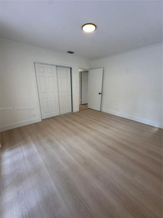 Room featuring wood-finish flooring, white walls, flush-mount ceiling lighting, and sliding panel closet doors