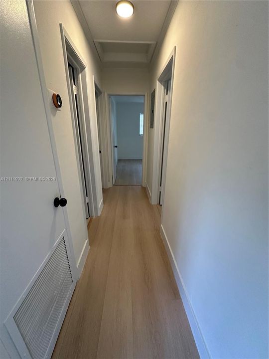 Hallway featuring light-toned wood-finish flooring, crisp white walls, flush-mount circular lighting, and matte black door hardware