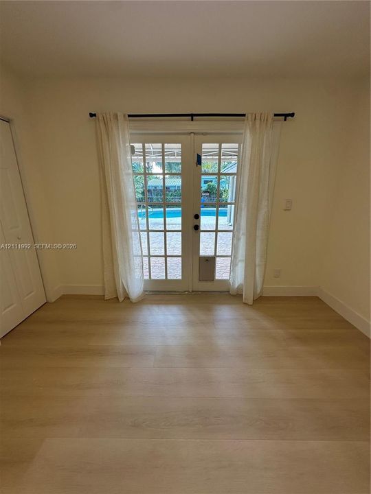 Interior space featuring wood-finish flooring, light-toned walls, and French doors leading to an exterior paved area with a swimming pool