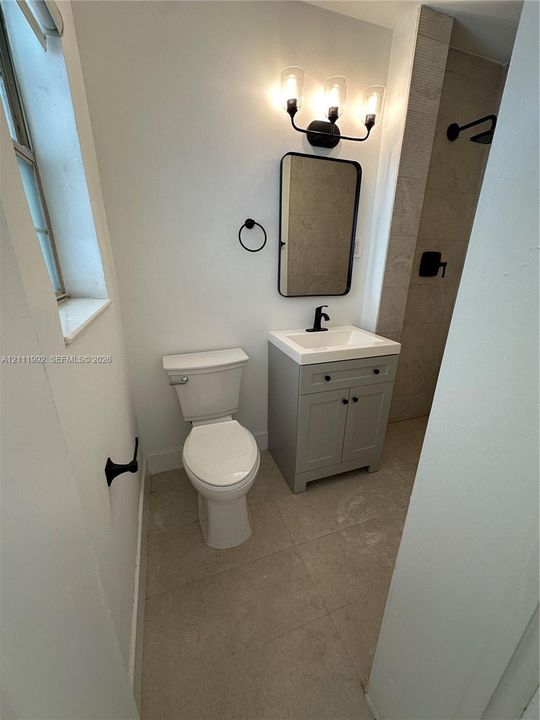 Bathroom featuring a grey vanity with a white countertop, matte black fixtures, a rectangular vanity mirror, and neutral-toned floor tile