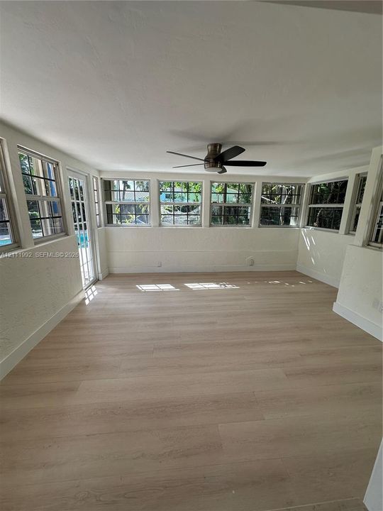 Sunroom featuring wood-finish flooring, a series of multi-pane windows, and an overhead ceiling fan