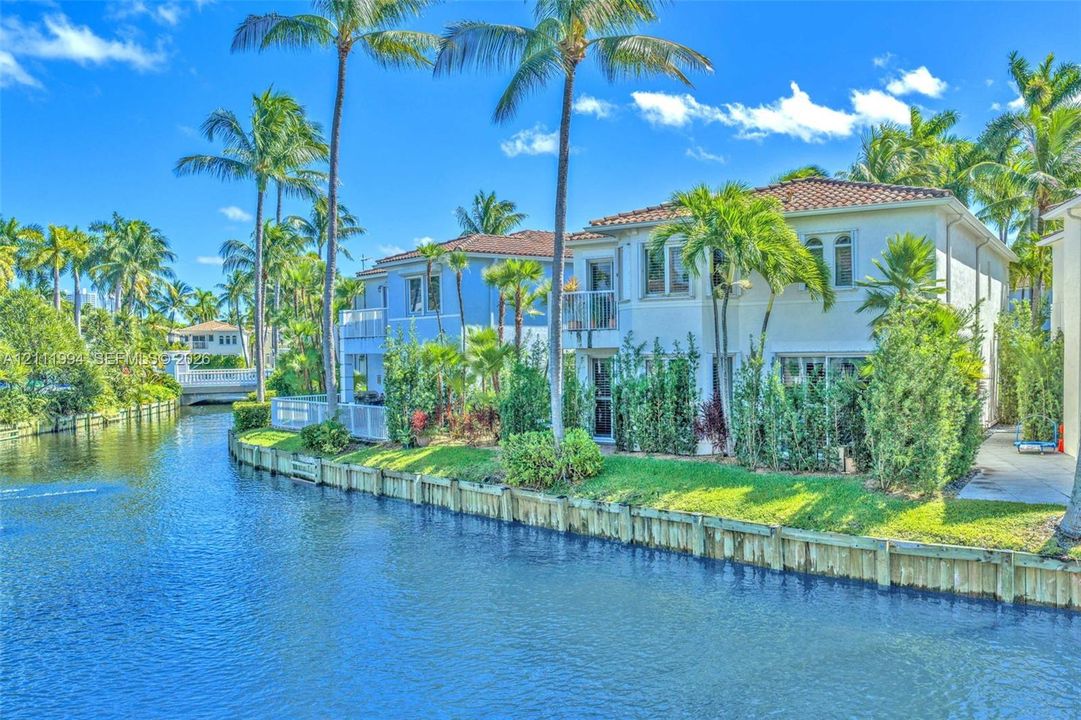 Waterfront property featuring a canal bulkhead, two-story structure with a terracotta tile roof, white stucco facade, and mature palm landscaping