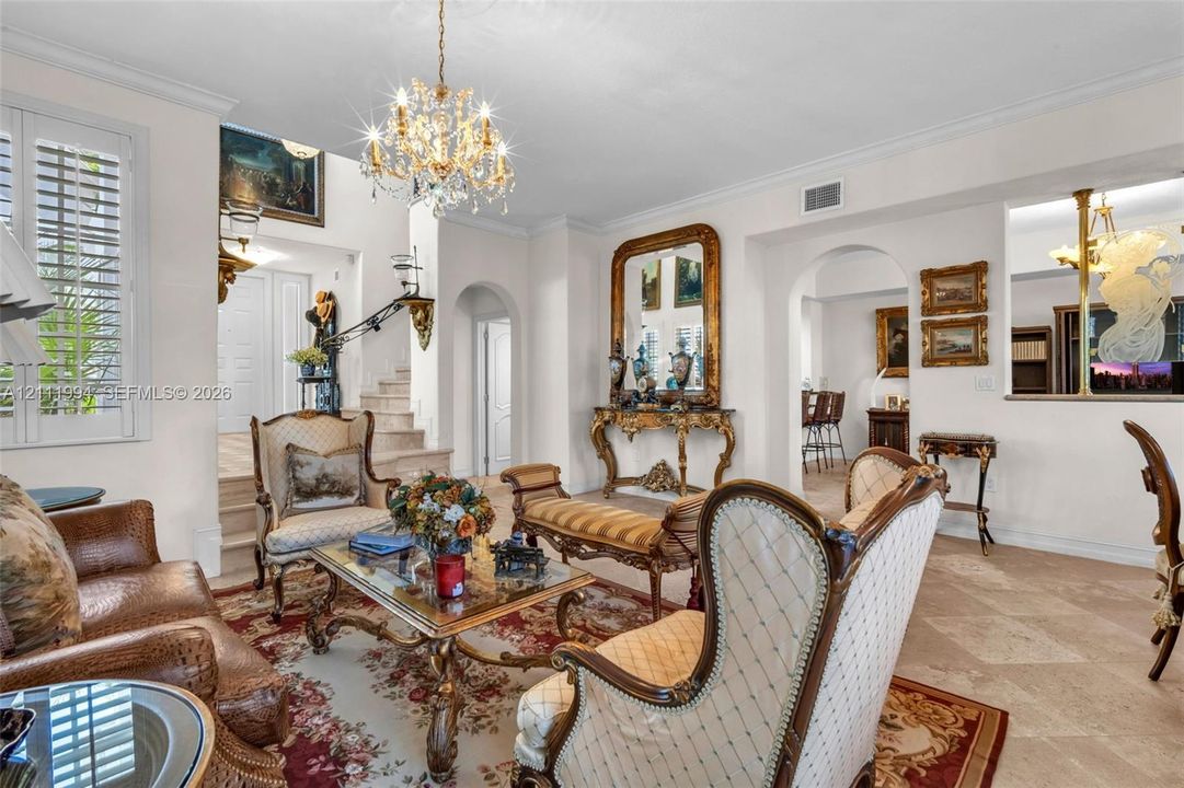 Living area featuring stone flooring, ornate crystal chandelier, arched doorways, crown molding, and plantation shutters