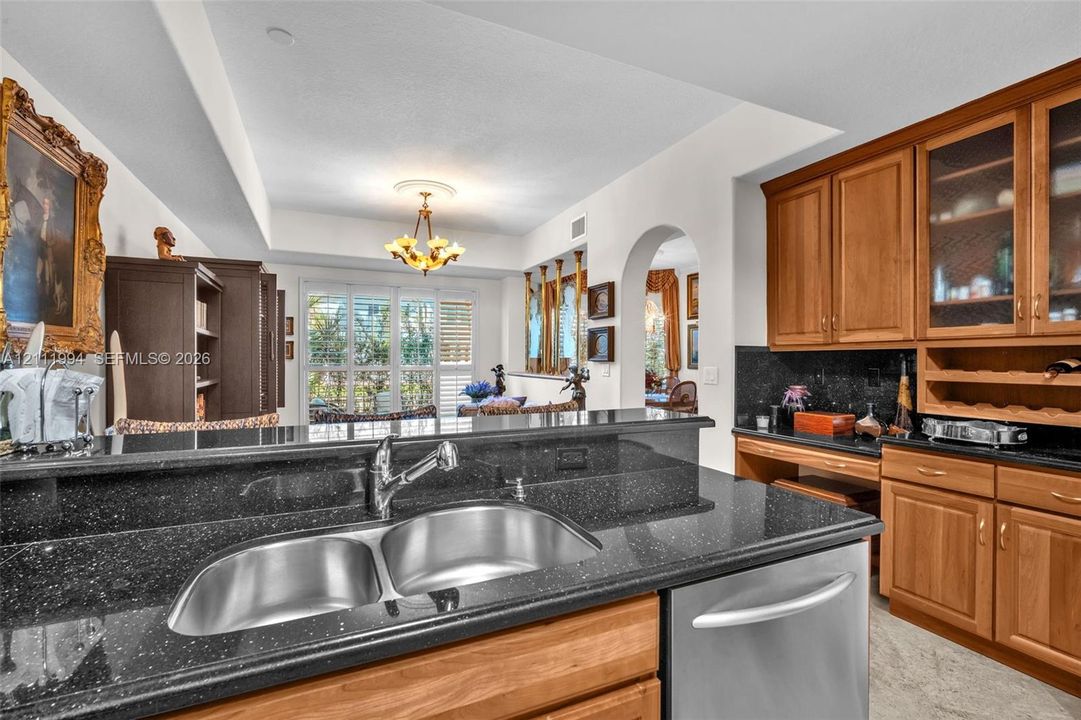 Kitchen featuring wood cabinetry, integrated wine storage, dark stone countertops, a dual-basin undermount sink, and stainless steel dishwasher
