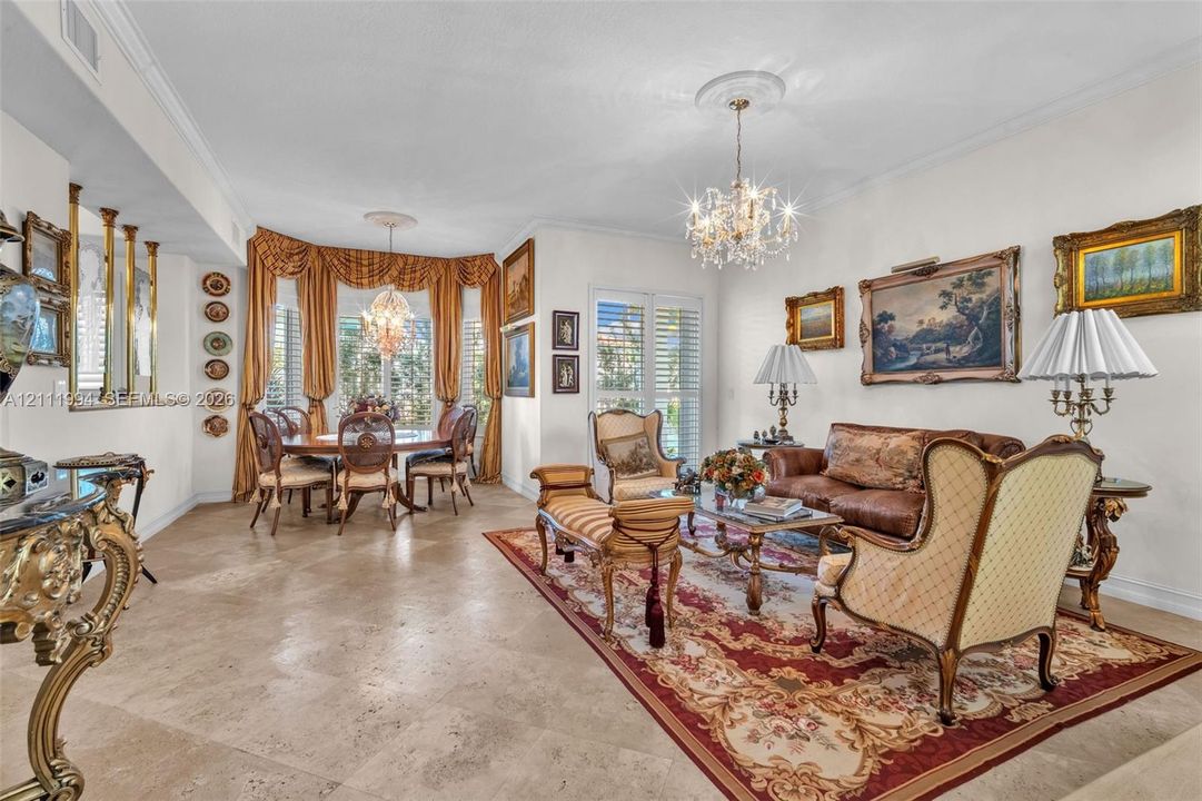 Open-concept area featuring stone flooring, ornate crystal chandeliers, floor-to-ceiling windows with crown molding, and decorative architectural pillars