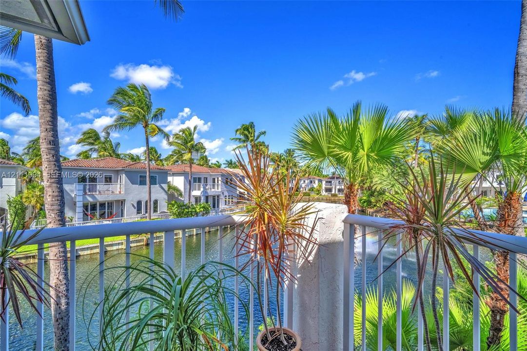 Private balcony with white metal railings overlooking a canal with mature palm trees and lush tropical landscaping
