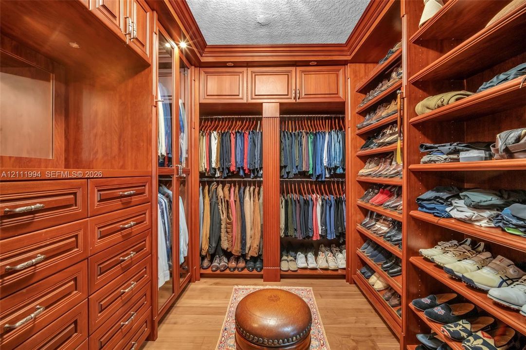 Custom walk-in closet featuring extensive cherry-toned wood cabinetry, built-in shelving, integrated hanging rods, glass-fronted wardrobe doors, and multiple tiers of drawers with metal hardware