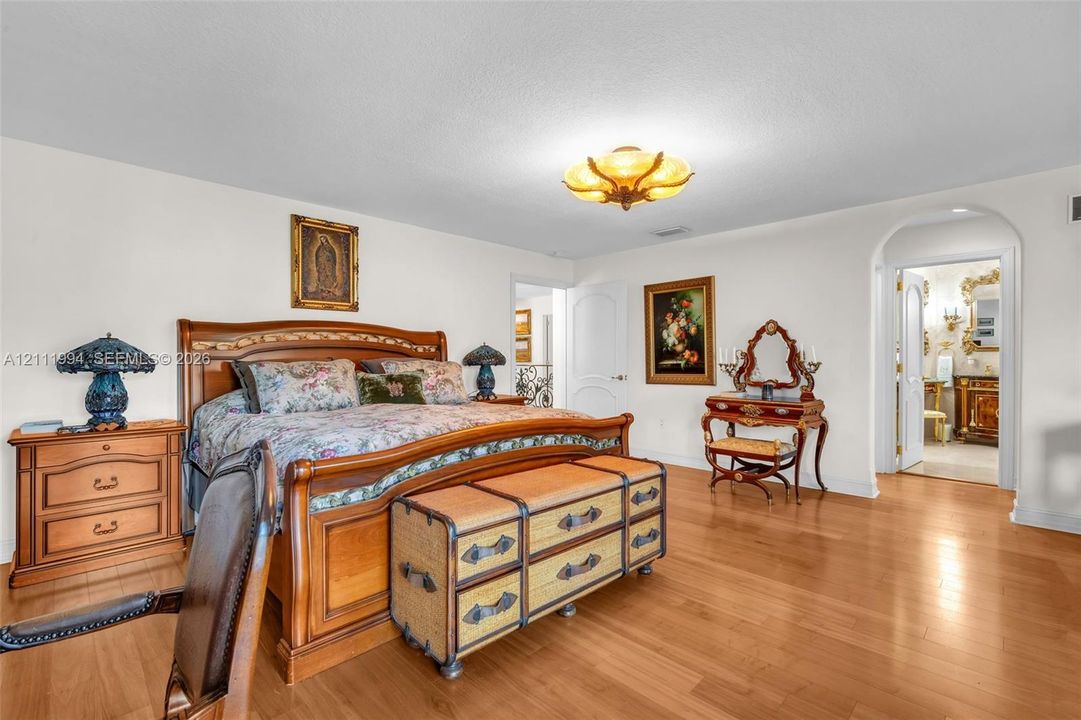 Spacious room featuring wood-finish flooring, a decorative multi-bulb flush mount ceiling fixture, and an arched doorway leading to a secondary room