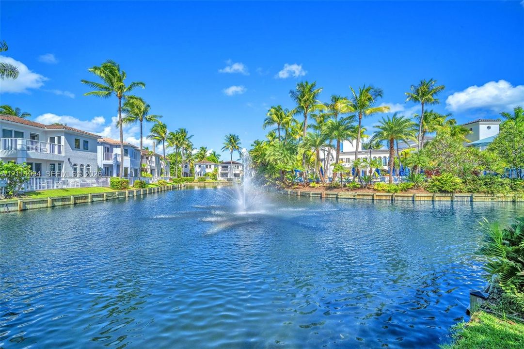 Manicured lakefront grounds featuring a central fountain, timber-framed bulkhead, and mature palm trees