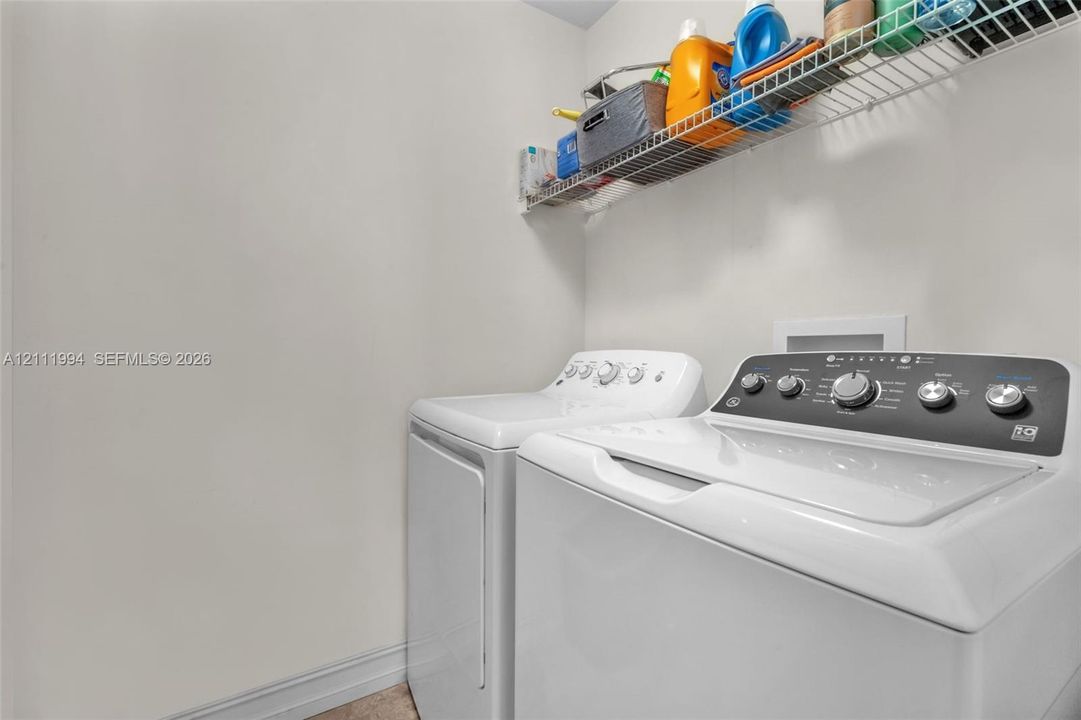 Laundry area equipped with top-load washer and dryer, featuring white finish cabinetry and overhead wire shelving