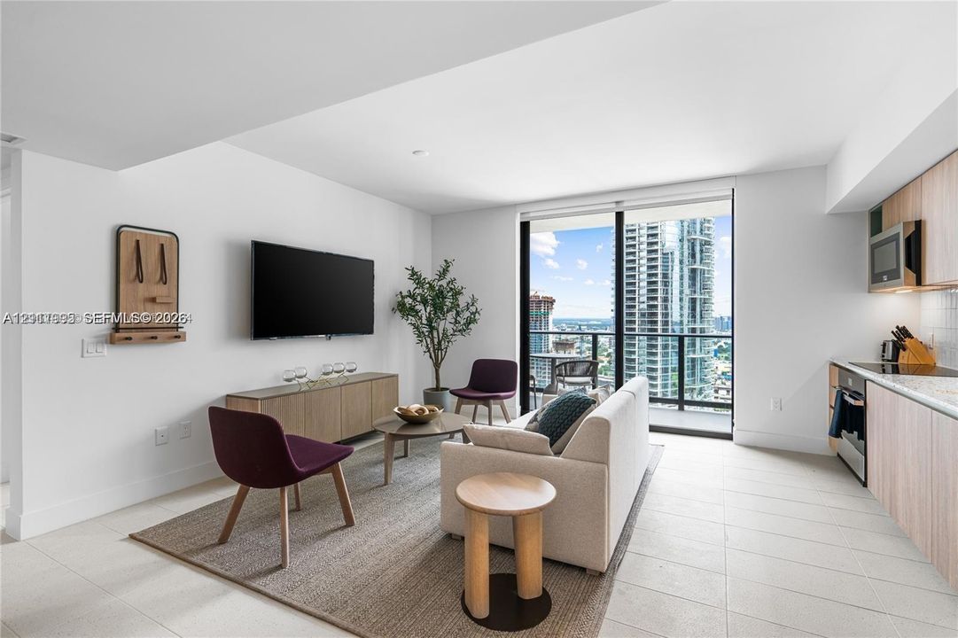 Open-concept living space featuring floor-to-ceiling windows, porcelain tile flooring, recessed lighting, and kitchen cabinetry with a light wood finish