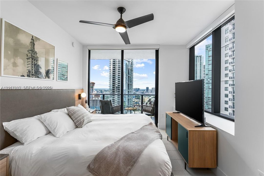 Floor-to-ceiling windows, private balcony, neutral wall tones, matte black ceiling fan, and tile flooring