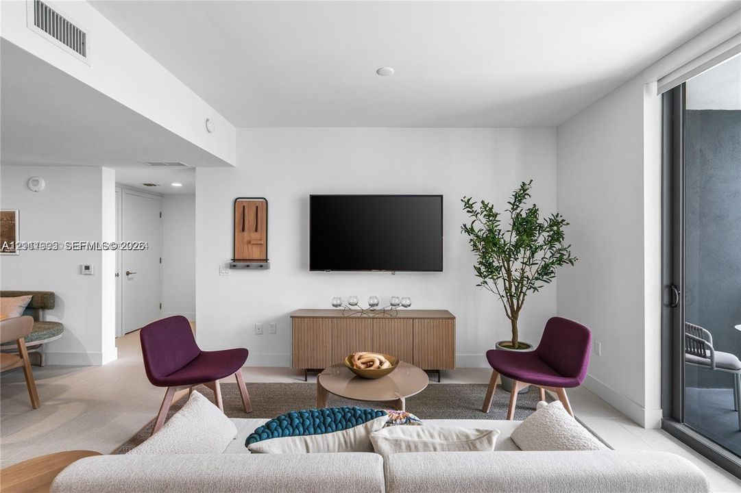 Neutral palette living area featuring light wood-finish flooring, white walls, and a glass sliding door providing exterior access