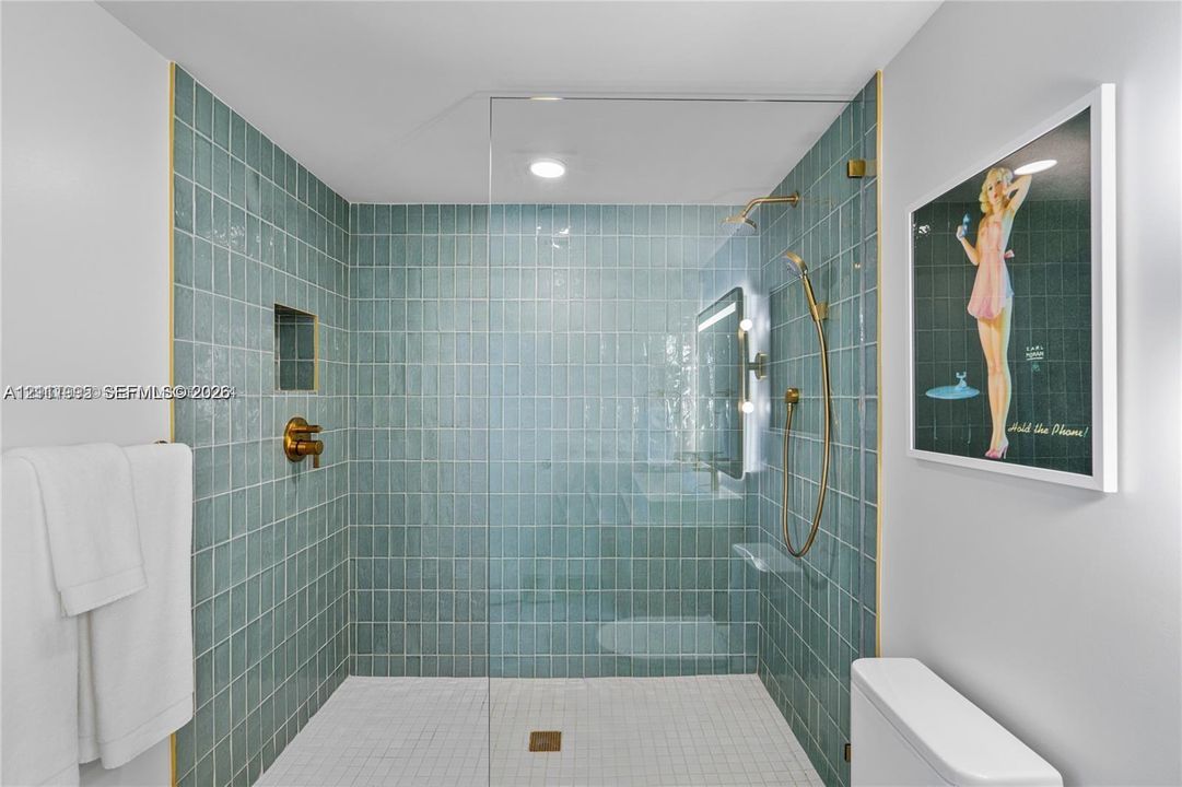 Walk-in shower featuring glossy teal wall tile, frameless glass enclosure, brass-finish rainfall shower head with handheld attachment, and built-in recessed wall niche