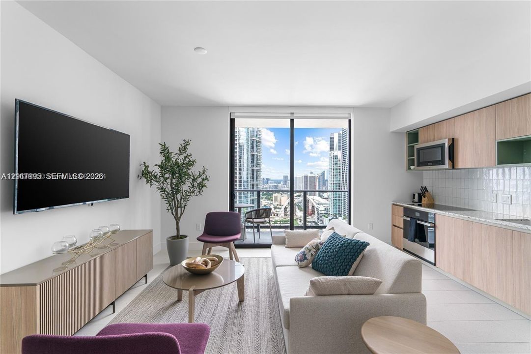Open-concept area featuring wood-finish cabinetry, built-in stainless steel appliances, tiled backsplash, large sliding glass doors, and floor-to-ceiling windows