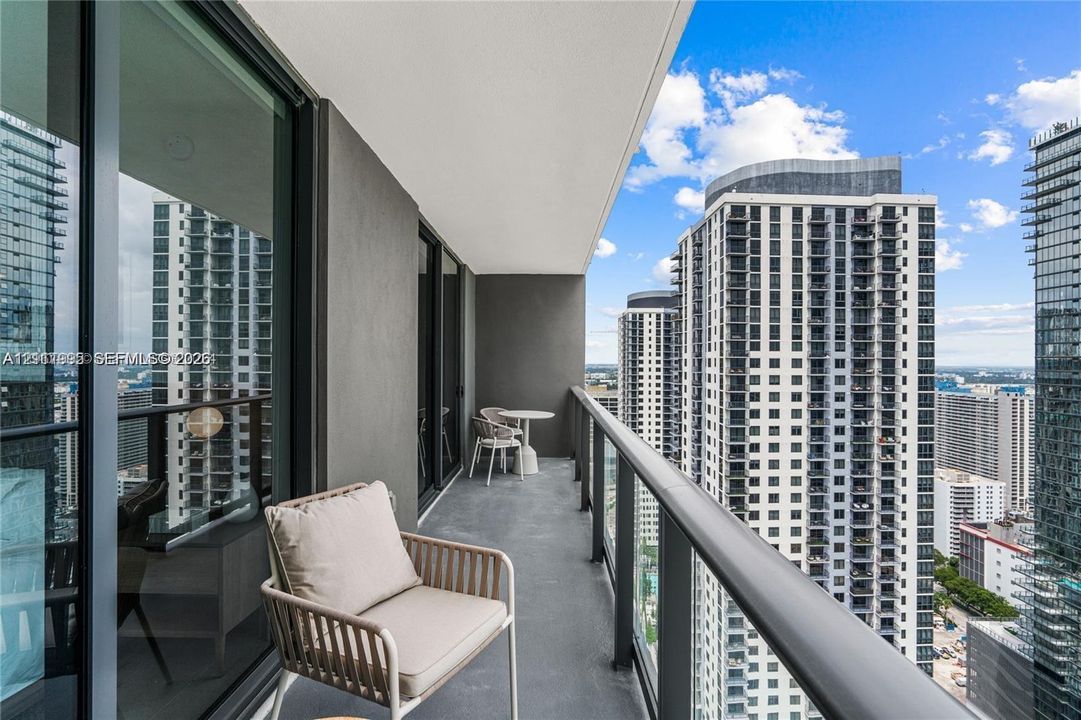 Private balcony with concrete flooring, floor-to-ceiling glass sliding doors, and a metal railing
