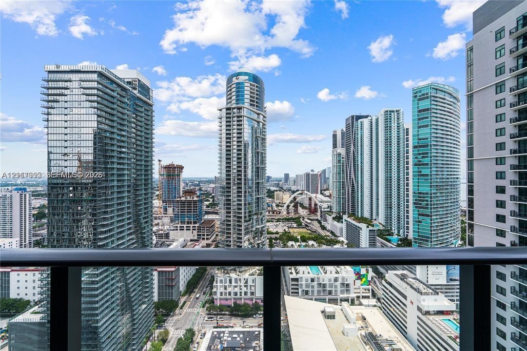Private balcony with a metal and glass railing overlooking a high-density urban cityscape