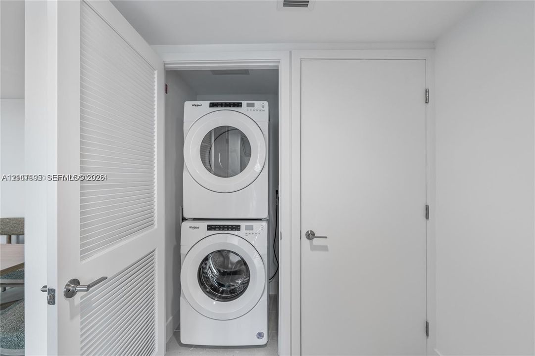 Stacked white front-load washer and dryer unit enclosed within a dedicated closet featuring a louvered door